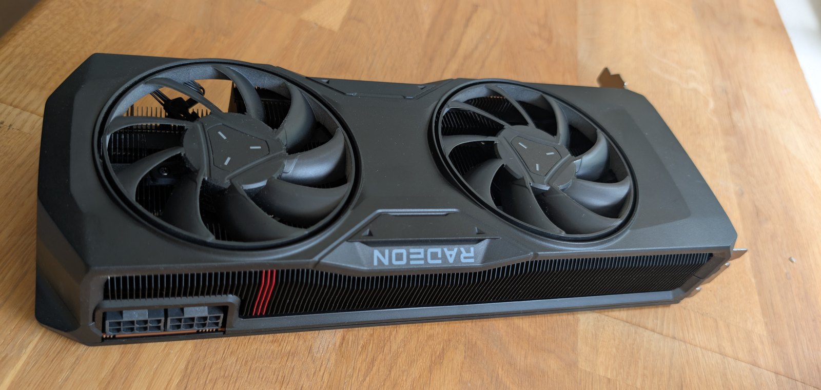 AMD Radeon RX 7800 XT reference-design graphics card, dual-fan cooler, photographed from above on a wooden desk.