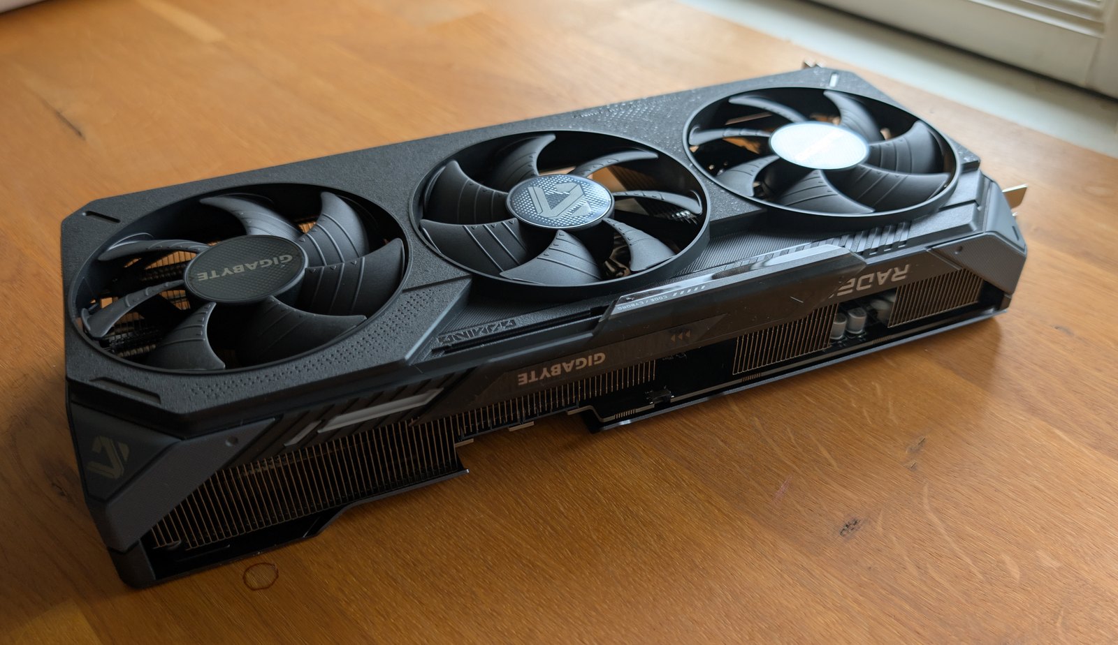 GIGABYTE Radeon RX 9070 GAMING OC graphics card, triple-fan cooler, photographed from above on a wooden desk.
